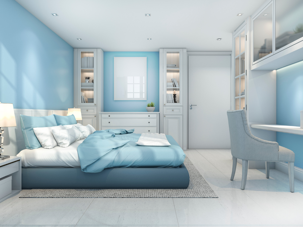 Cozy & Stylish Bedroom Flooring Ideas 3 Modern bedroom with blue walls, a double bed with blue and white bedding, built-in shelves, sleek bedroom flooring, a desk with a chair, and a door at the back. The room is bright and neatly organized.