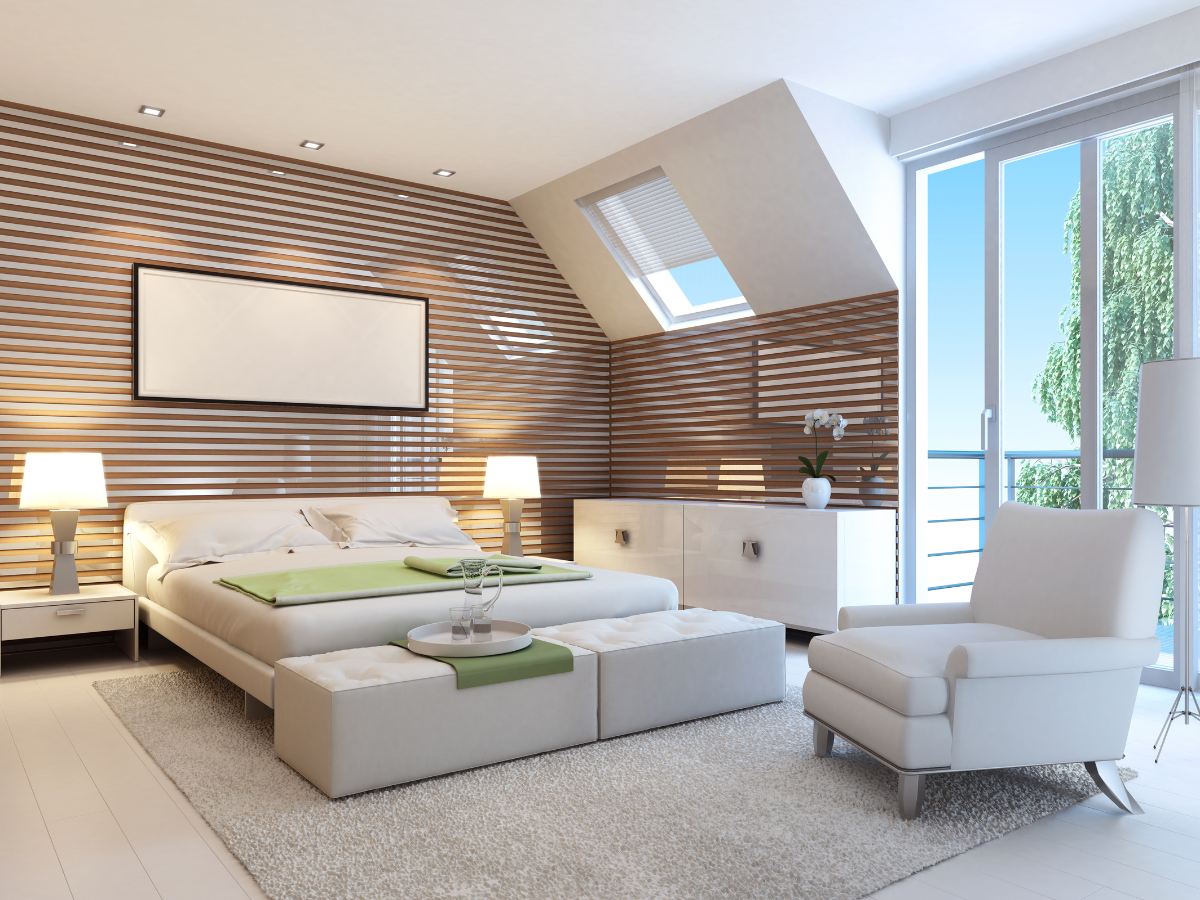 Modern bedroom with a large bed, white furniture, a cozy rug atop stylish bedroom flooring, wood panel accent wall, and ample natural light from a window and glass door leading to a balcony.
