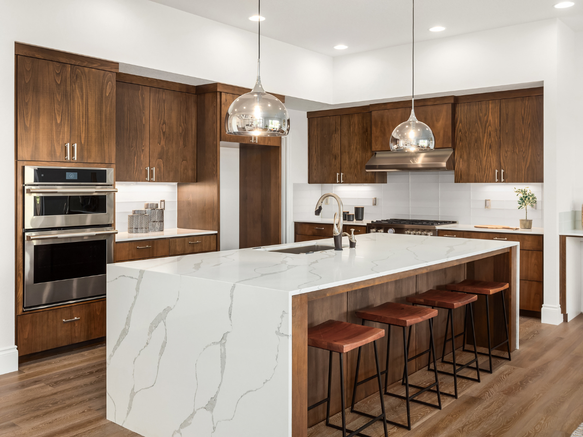 Frequently Asked Questions About Flooring: Answers to Your Top Questions 4 Modern kitchen with wood cabinets, a large white marble island with sink, pendant lights, stainless steel appliances, and four brown stools—perfect for gatherings or entertaining guests. For more details about design choices and materials used in this space, please see our Frequently Asked Questions.