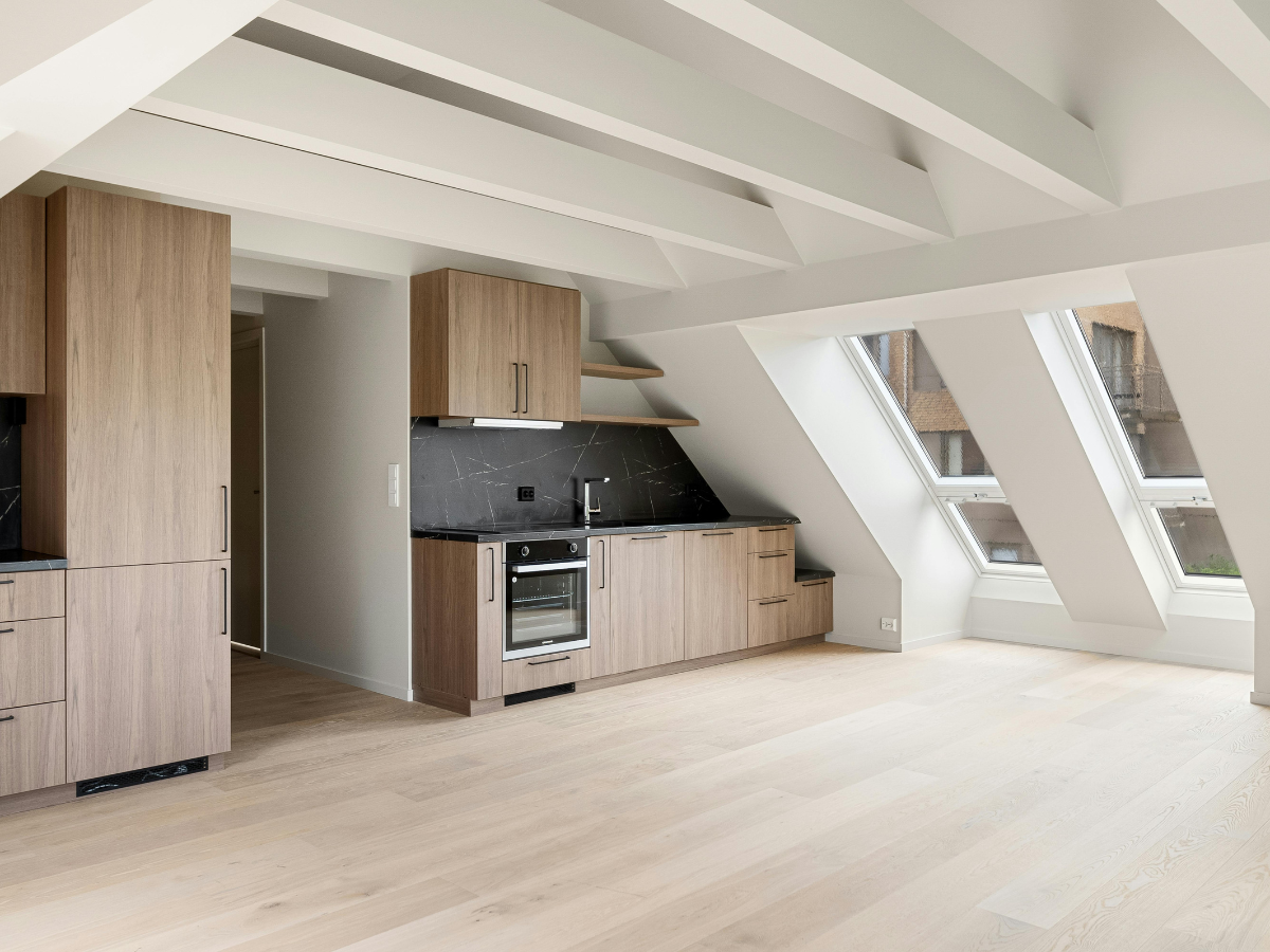 Frequently Asked Questions About Flooring: Answers to Your Top Questions 6 Modern attic kitchen with light wood cabinets, black countertops, built-in appliances, sloped ceiling, and large windows letting in natural light—explore our Frequently Asked Questions to learn more about designing and optimizing such unique spaces.