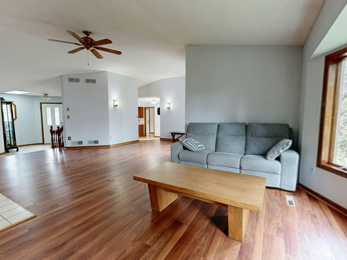 Frequently Asked Questions About Flooring: Answers to Your Top Questions 1 Spacious living room with wood flooring, gray sofa, wooden coffee table, ceiling fan, large windows, and light gray walls—designed to answer all your Frequently Asked Questions about comfort and style in modern interiors.