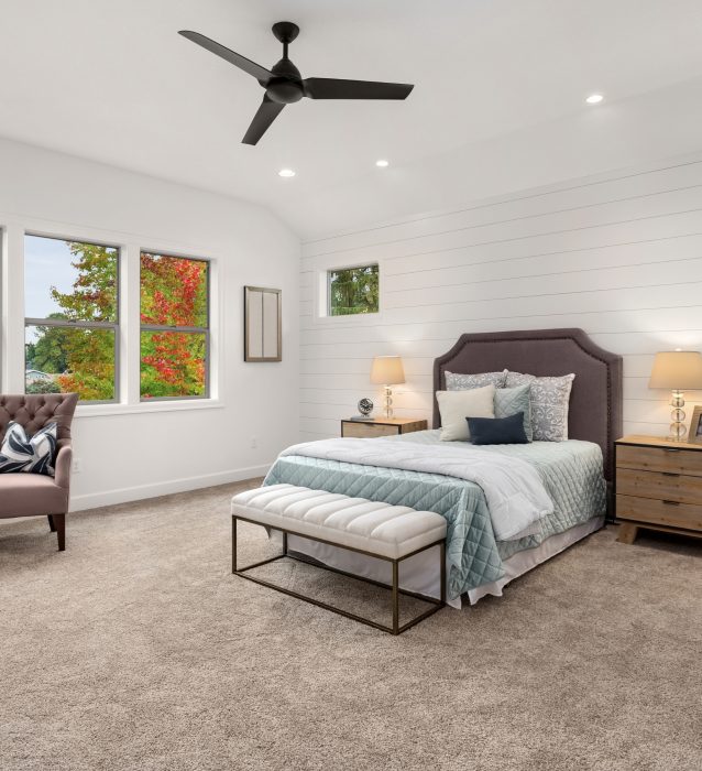 A bedroom with beige walls and a ceiling fan undergoing carpet installation.
