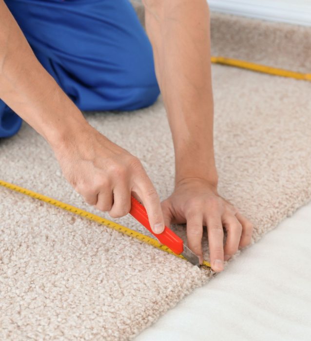 A man measuring carpet for installation using a tape measure.