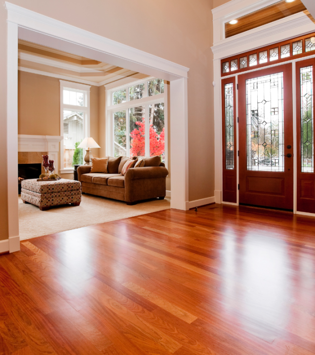 Elegant living room with polished hardwood floors, cozy couch, decorative ottoman, and large windows showcasing vibrant autumn foliage, highlighting the inviting atmosphere of a transformed space by Diaz Hardwood Floors.