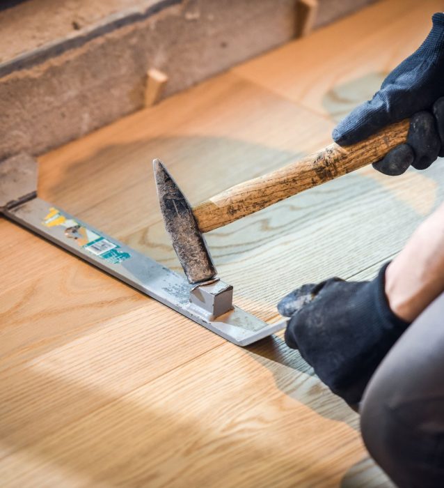 A man is hammering hardwood flooring.